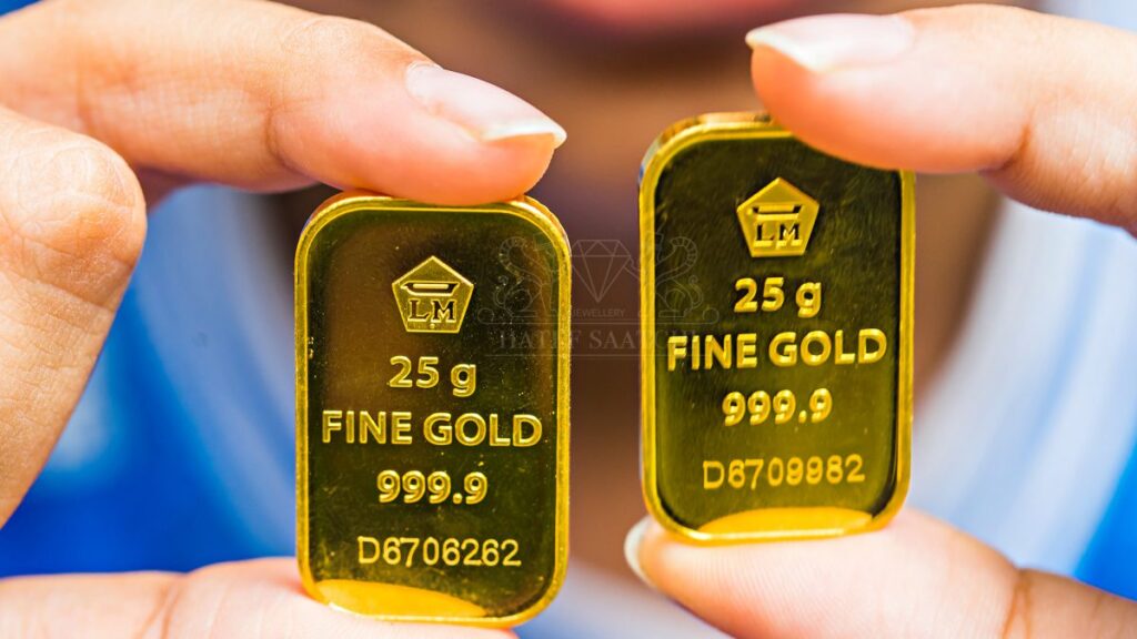 تصویر دست یک نفر که دو قطعه شمش طلا 25 گرمی را رو به دوربین گرفته است و عیار طلا در آن مشخص شده است