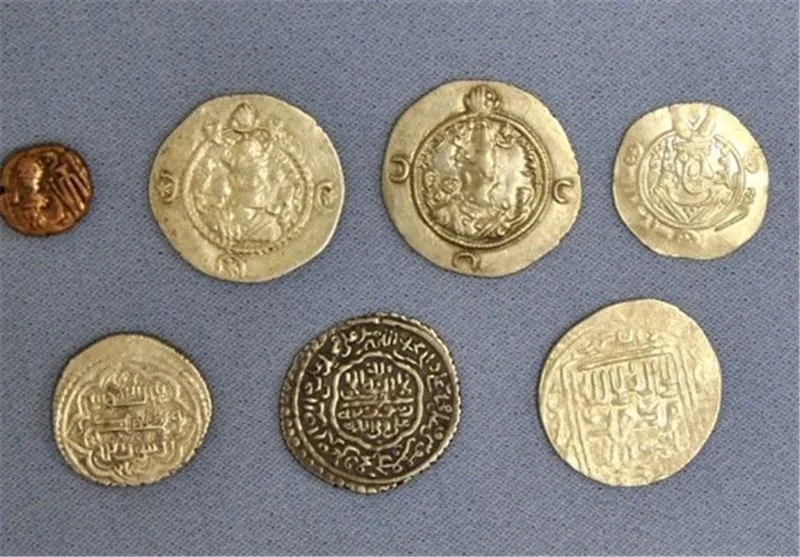 نمای بالا از ۷ سکه طلا از انواع سکه های قدیمی ایران بر پس‌زمینه آبی‌رنگ
