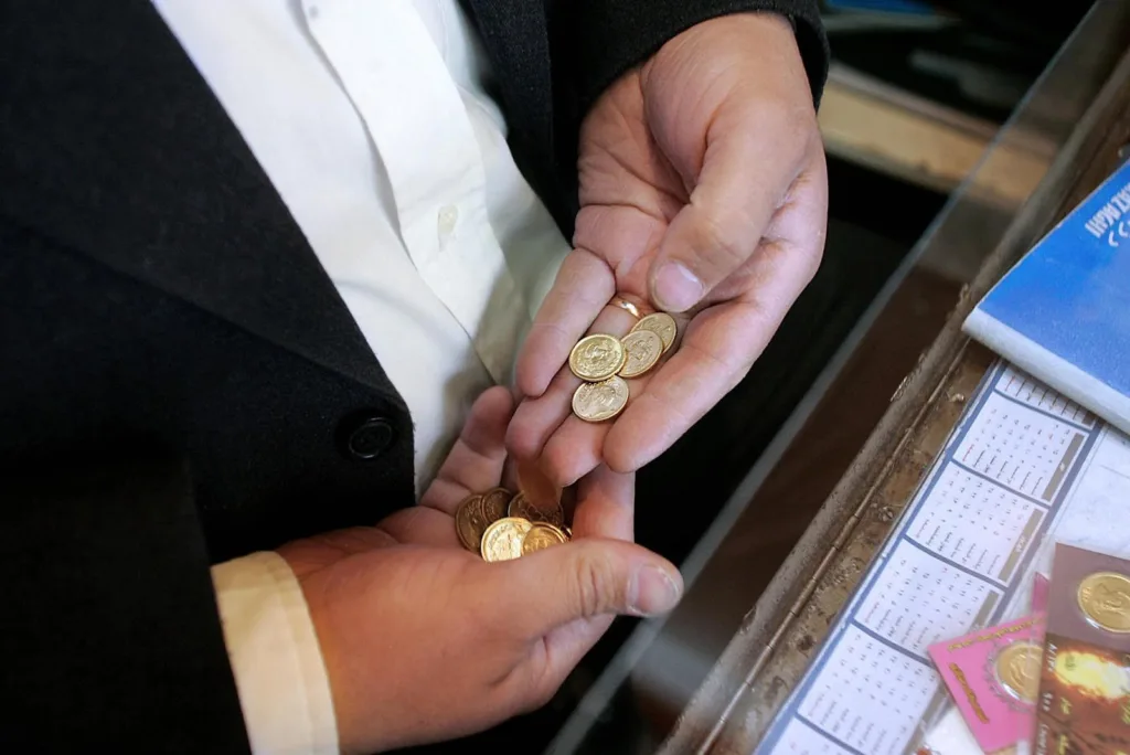 دستان یک مرد بازاری در حال بررسی تعدادی سکه پارسیان