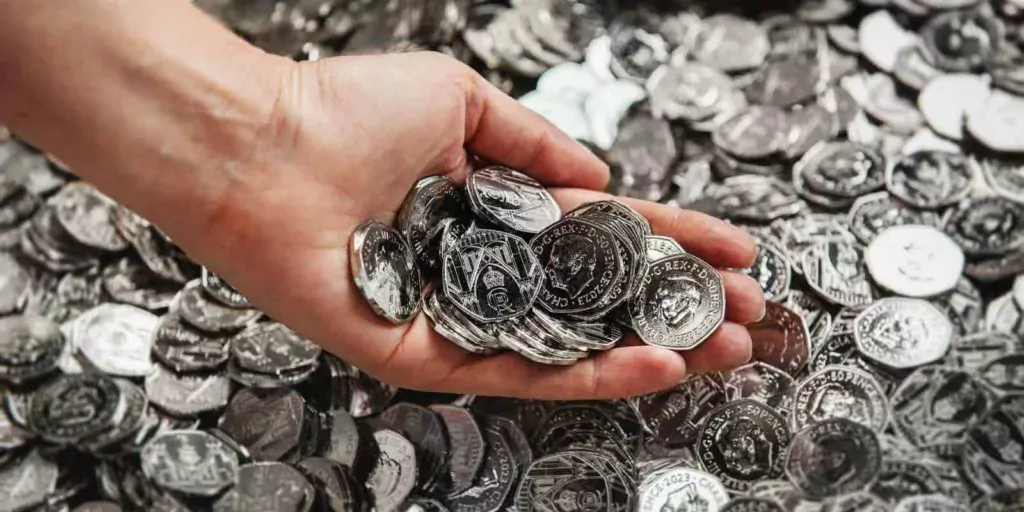 نمای بالا از دست چپ یک سرمایه‌گذار در حال برداشتن تعدادی سکه نقره از میان تعداد بسیار زیاد سکه نقره