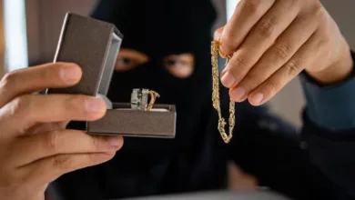 نمای روبه‌رو از دزدی با صورت پوشیده در حال دزدیدن انگشتر طلا و دستبند از خانه
