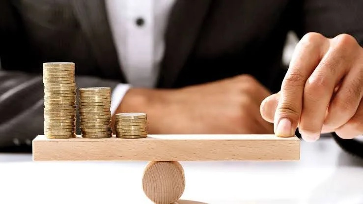 نمای روبه‌رو از گردن به پایین یک مرد سرمایه‌گذار در حال انتخاب بهترین سکه برای سرمایه‌گذاری است که مقابل او چند سکه با ارتفاع مختلف روی یک تخته چوبی قرار دارد.