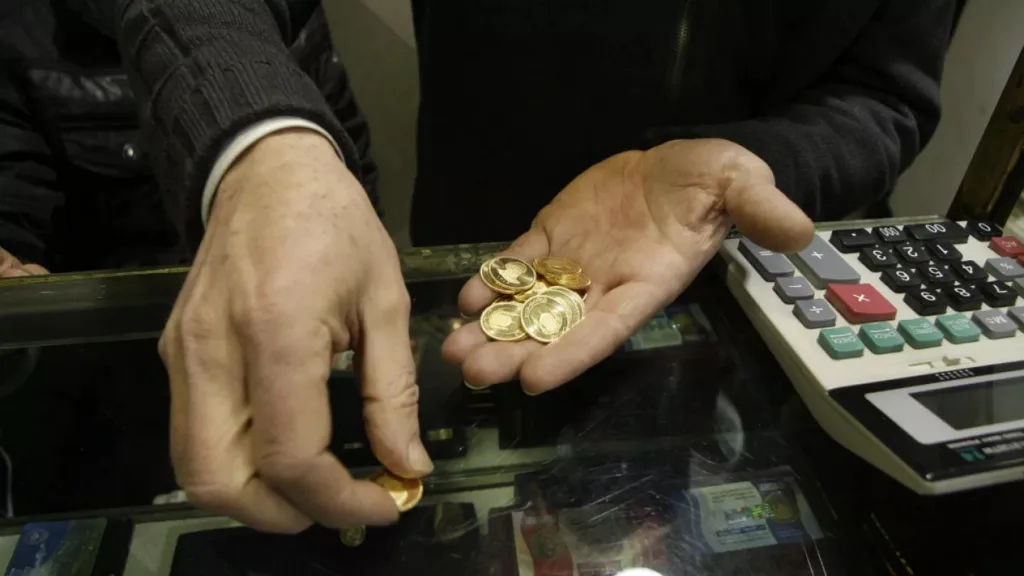 سکه‌های طلا در دست آقا و یک ماشین حساب کنارش