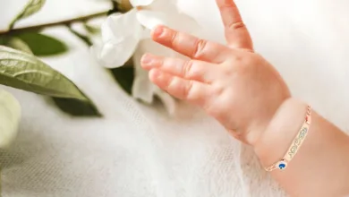 دست یک نوزاد تپل که چهار انگشت آن پیداست و پس زمینه آن سفید رنگ است و یک دستبند طلا روی دست نوزاد وجود دارد.