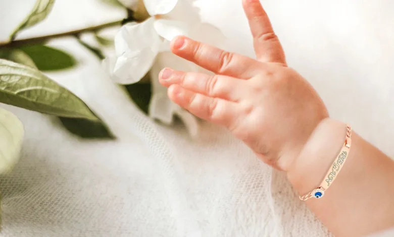 دست یک نوزاد تپل که چهار انگشت آن پیداست و پس زمینه آن سفید رنگ است و یک دستبند طلا روی دست نوزاد وجود دارد.