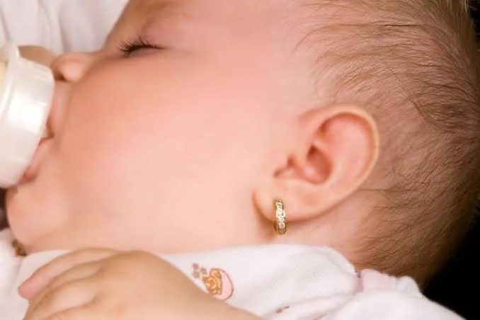 نمای بالا از صورت نوزادی با گوشواره طلا در حالت خوابیده و خوردن شیشه شیر