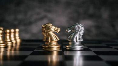 نمای روبه‌رو از یک صفحه شطرنج با دو مهره اسب به رنگ نقره و طلا در مقابل یکدیگر