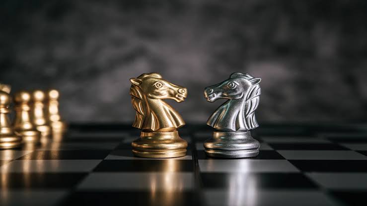 نمای روبه‌رو از یک صفحه شطرنج با دو مهره اسب به رنگ نقره و طلا در مقابل یکدیگر